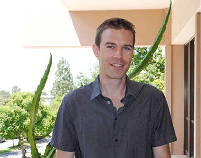 Man in short black hair wearing a grey short button up.