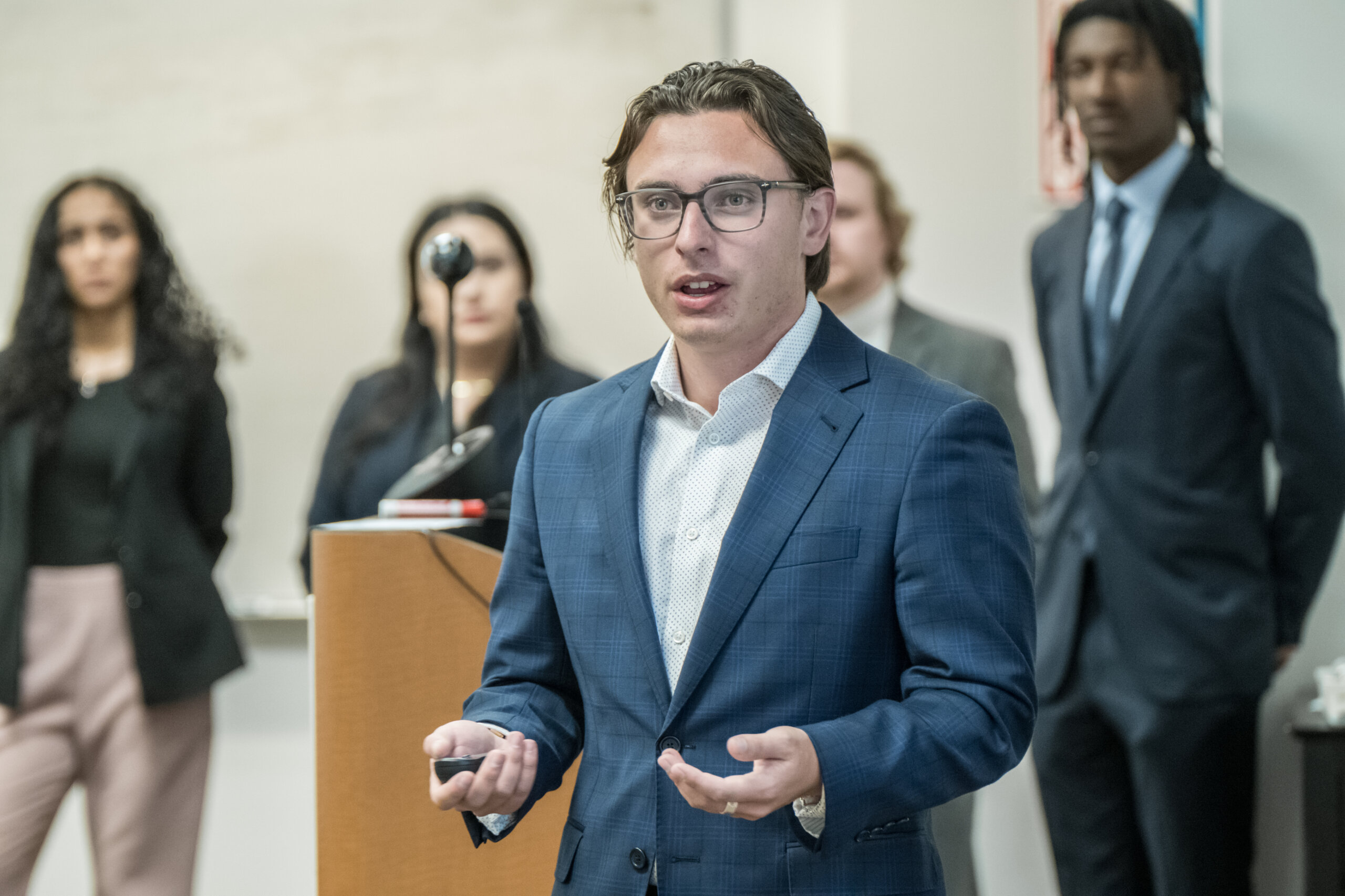 a student gives a presentation with his team standing behind him in a classroom