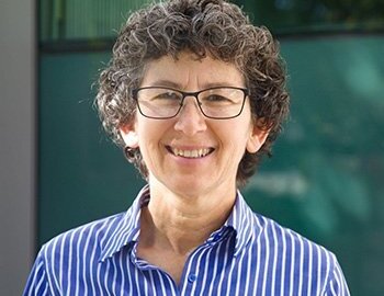 portrait of a woman with short brown h air, black glasses wearing a blue and white striped collared shirt.