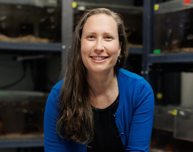 Woman in blue cardigan and black blouse with long light brown hair smiling.
