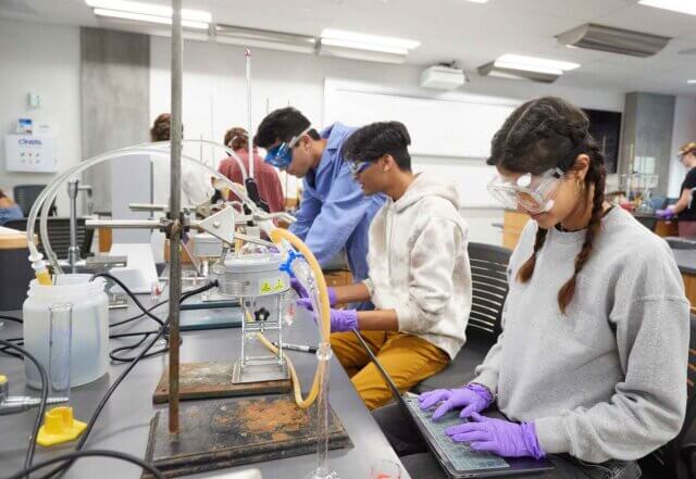 three students work on an experiment in a chemistry lab